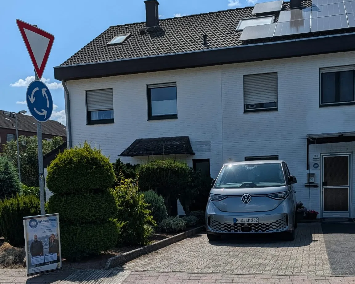 Das Elektrofahrzeug des Fahrdienstes steht abfahrbereit in der Einfahrt am Standort, daneben der Aufsteller des Fahr- und Botendienstes